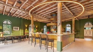 A rustic bar area with wooden beams, a circular light fixture, and a green wall with framed artwork. - Temple Tree at Bon Ton (Langkawi)