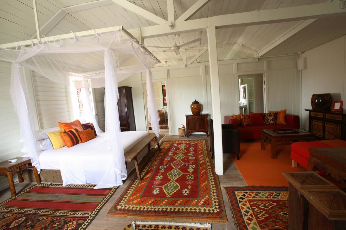 A room with a four-poster bed, a red and green patterned rug, a red sofa, and a wooden coffee table.