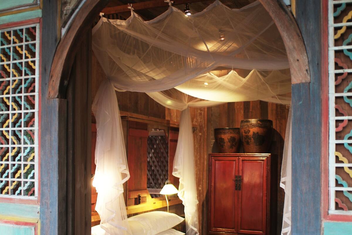 A room with a canopy bed, wooden furniture, and a decorative wall.
