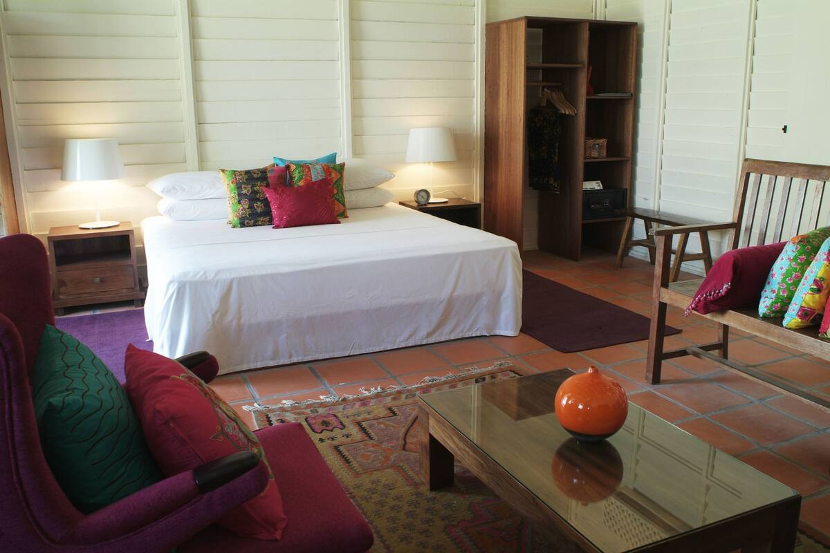 A hotel room with a bed, two bedside tables with lamps, a wooden wardrobe, a chair, and a coffee table with a vase.