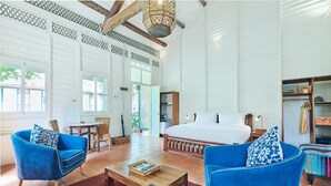 A spacious room with a large bed, two blue armchairs, a wooden coffee table, and a bookshelf. - Temple Tree at Bon Ton (Langkawi)