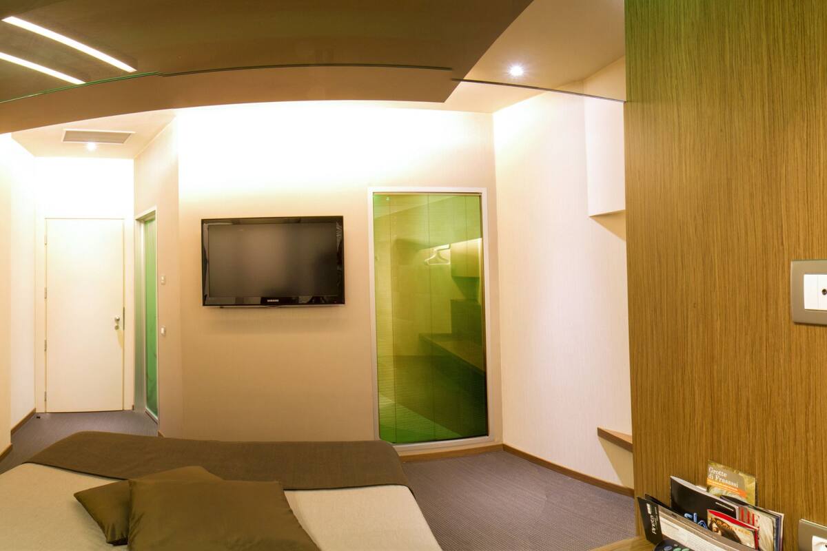 A modern hotel room with a bed, a flat-screen TV, and a green sliding door.