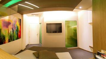 A modern hotel room with a bed, a flat-screen TV, and a green sliding door.