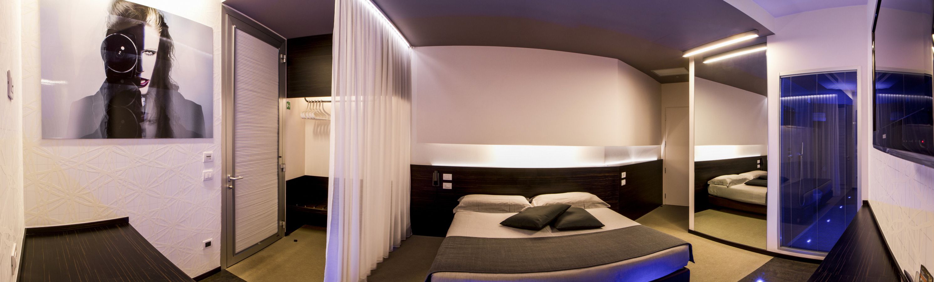 A modern hotel room with a curved ceiling, a large bed with a dark headboard, a bedside table, and a mirror.
