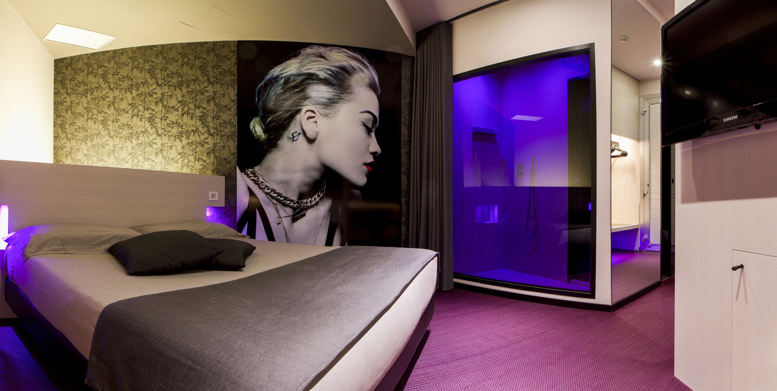 Una habitación de hotel moderna con una cama grande, un baño con cabina de ducha de vidrio y un televisor de pantalla plana.