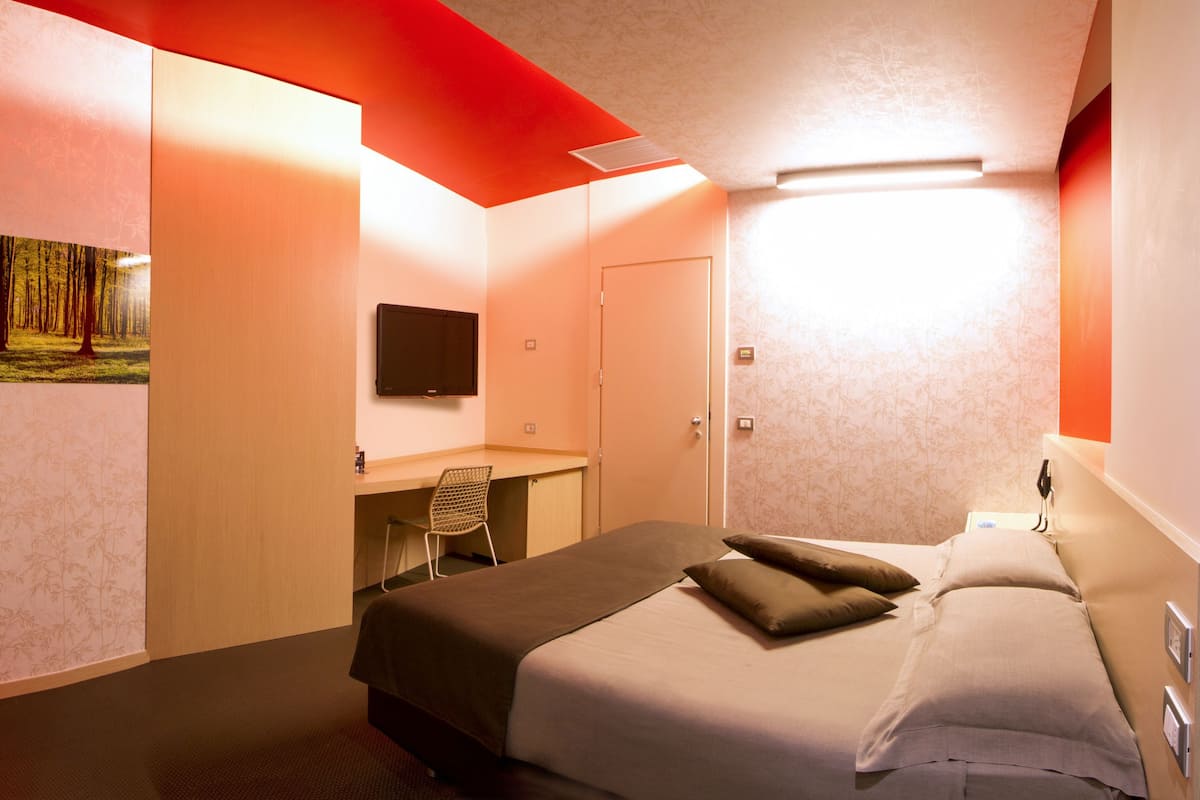 A hotel room with a bed, a desk, a chair, and a TV mounted on the wall.