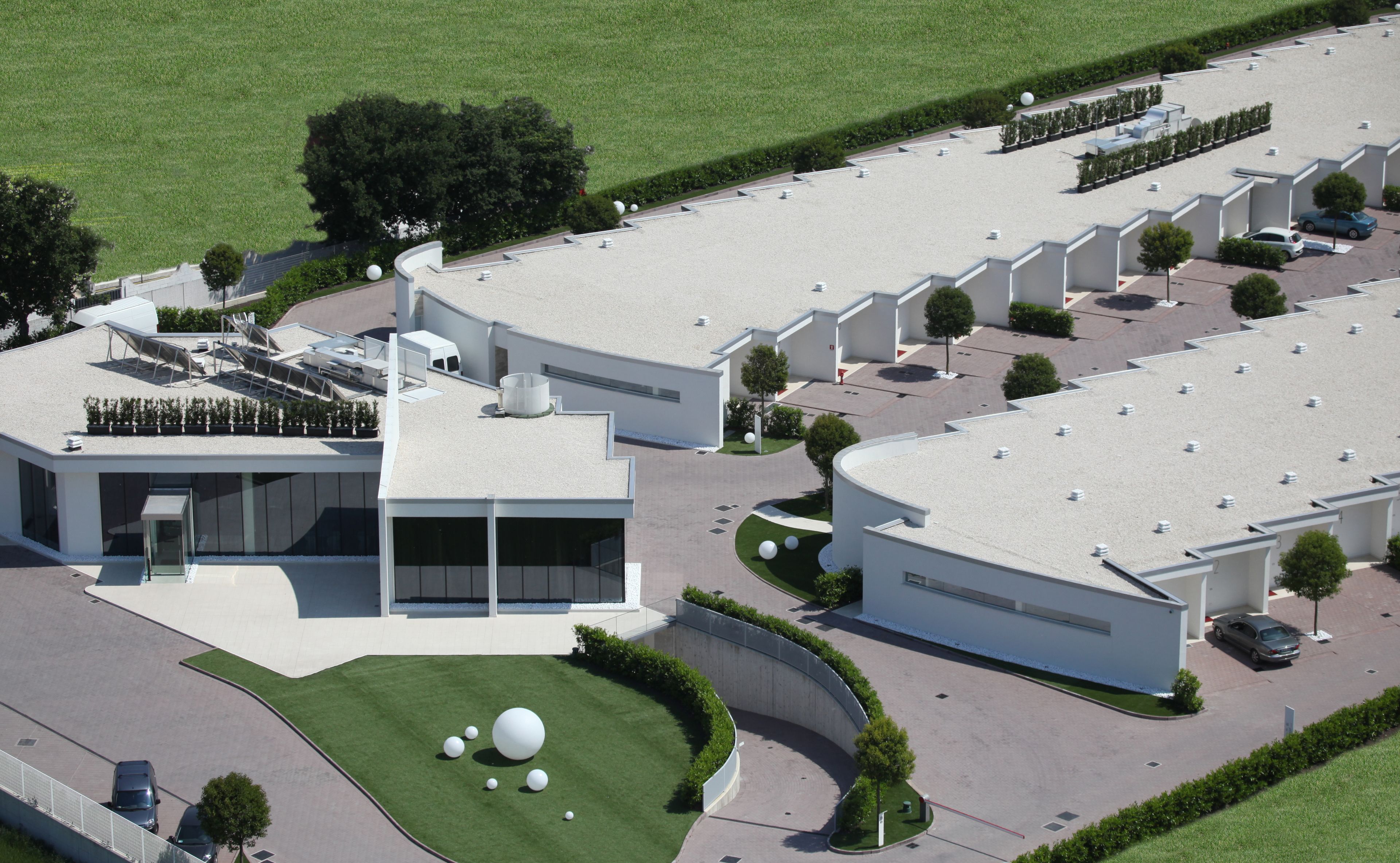 A modern building with a curved driveway, a parking area, and a landscaped garden with spherical sculptures.