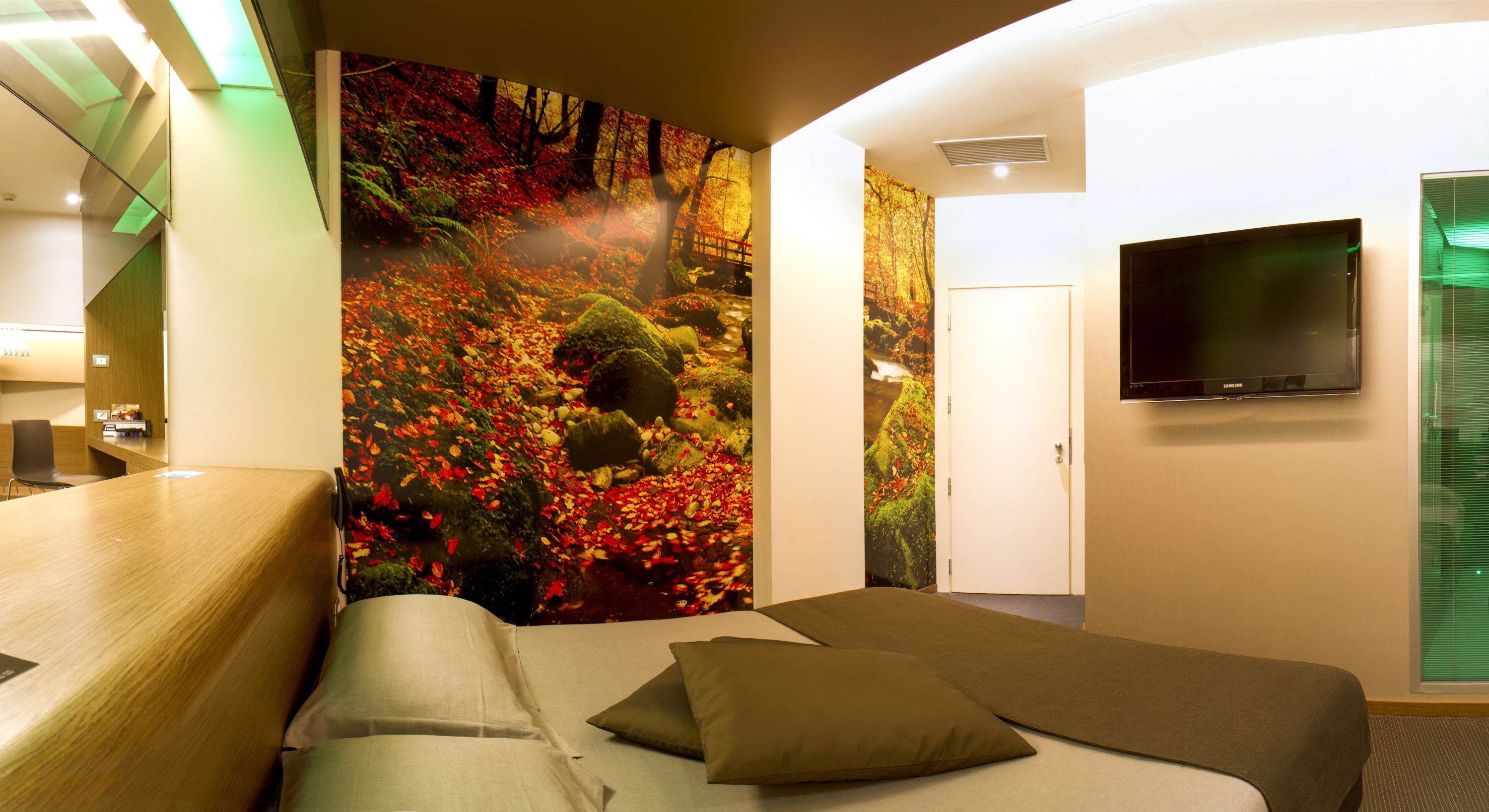 Ein Hotelzimmer mit einem Bett, einem Fernseher, einem Schreibtisch und einer großen Wandmalerei mit Waldbild.