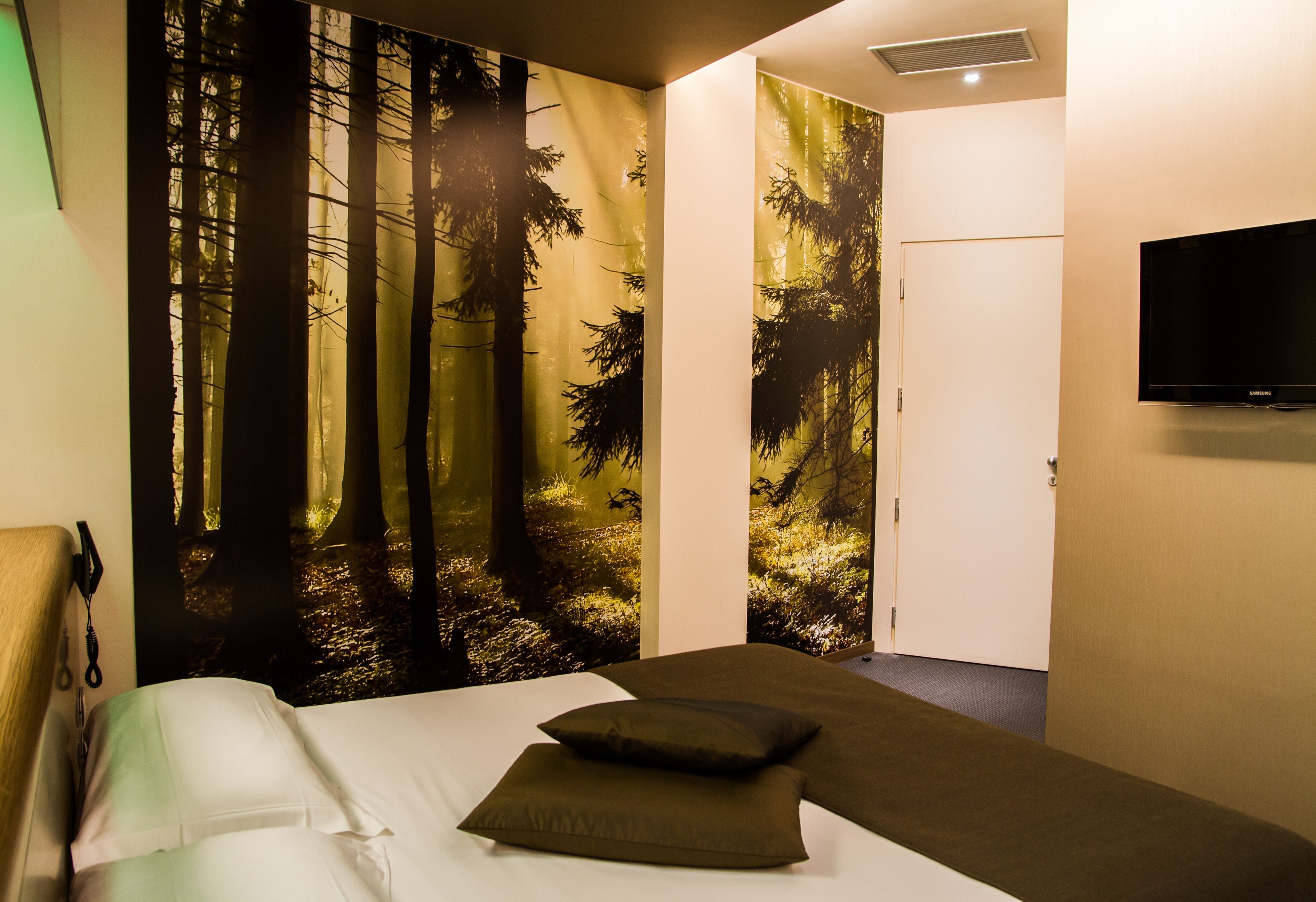 A bedroom with a bed, pillows, a wall-mounted TV, and a door.