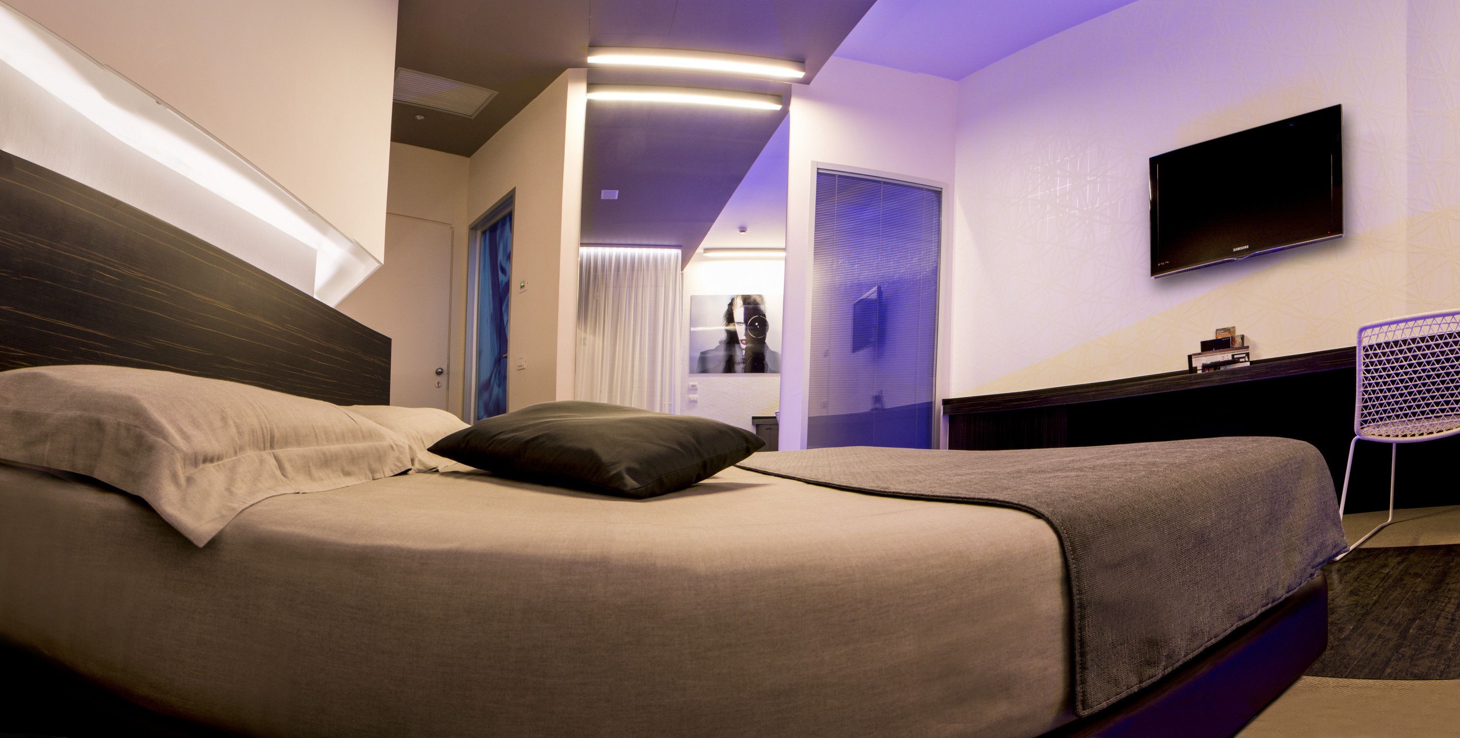 A modern hotel room with a bed, a flat-screen TV, a desk, and a chair.