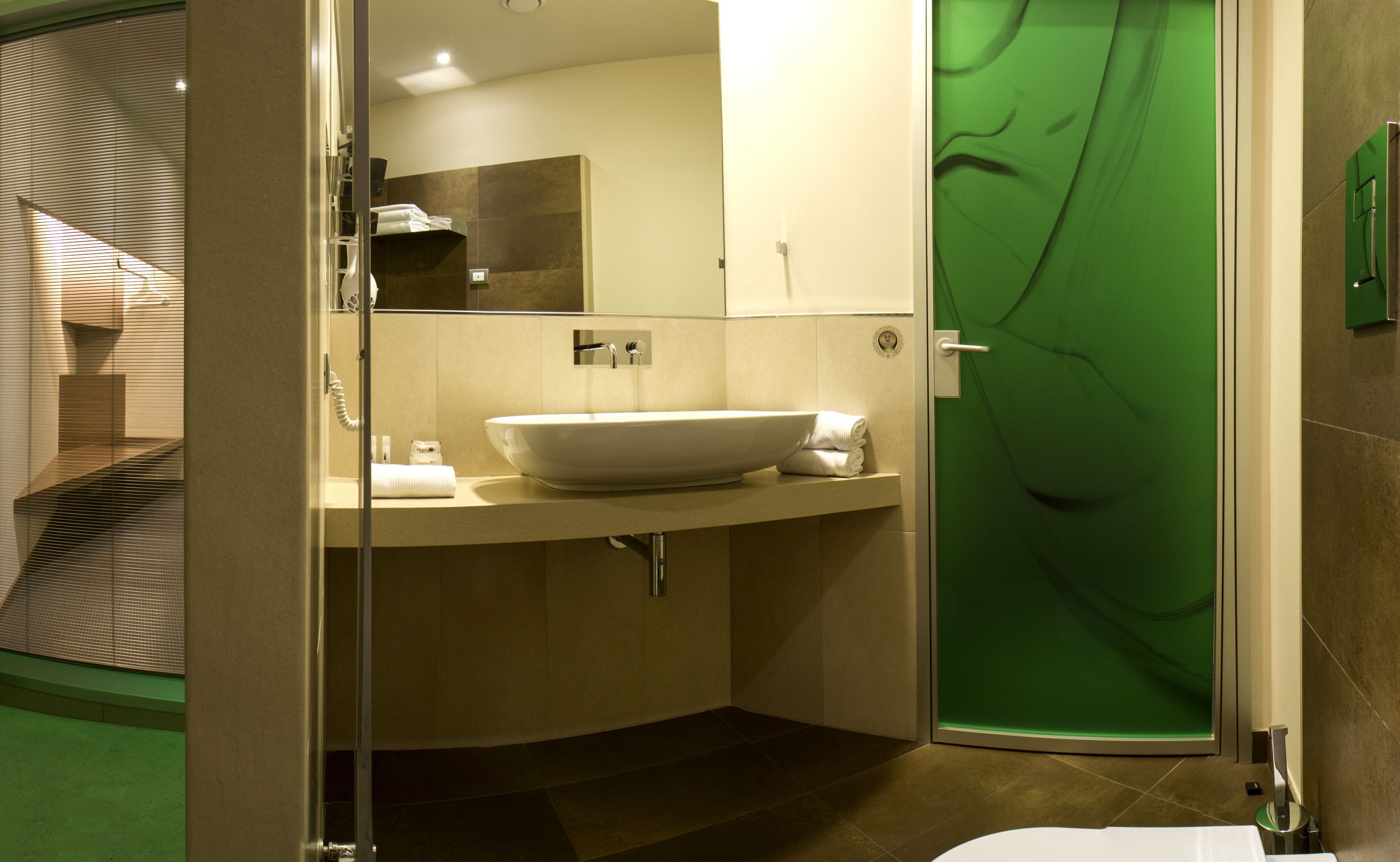 A modern bathroom with a large white sink, a mirror, and a green glass shower door.