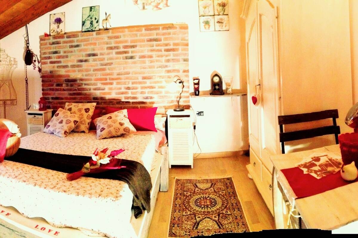 A cozy room with a bed, a television, a wooden table, and a brick wall.
