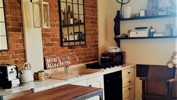 Eine Küche mit Backsteinwand, hölzernen Barhocker, einer hängenden Laterne und einem Schild mit der Aufschrift 'Mom's Kitchen'.