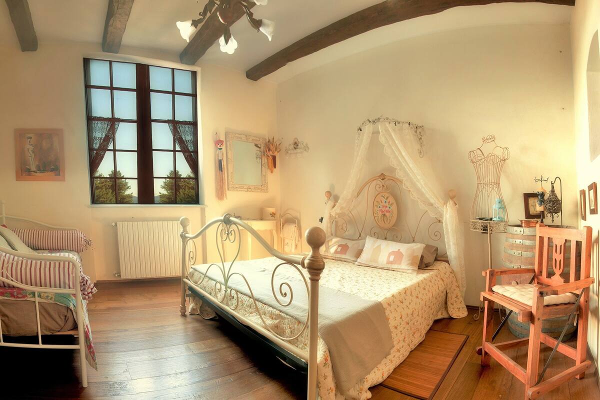A bedroom with a large window, a bed with a canopy, a wooden chair, and a dresser.