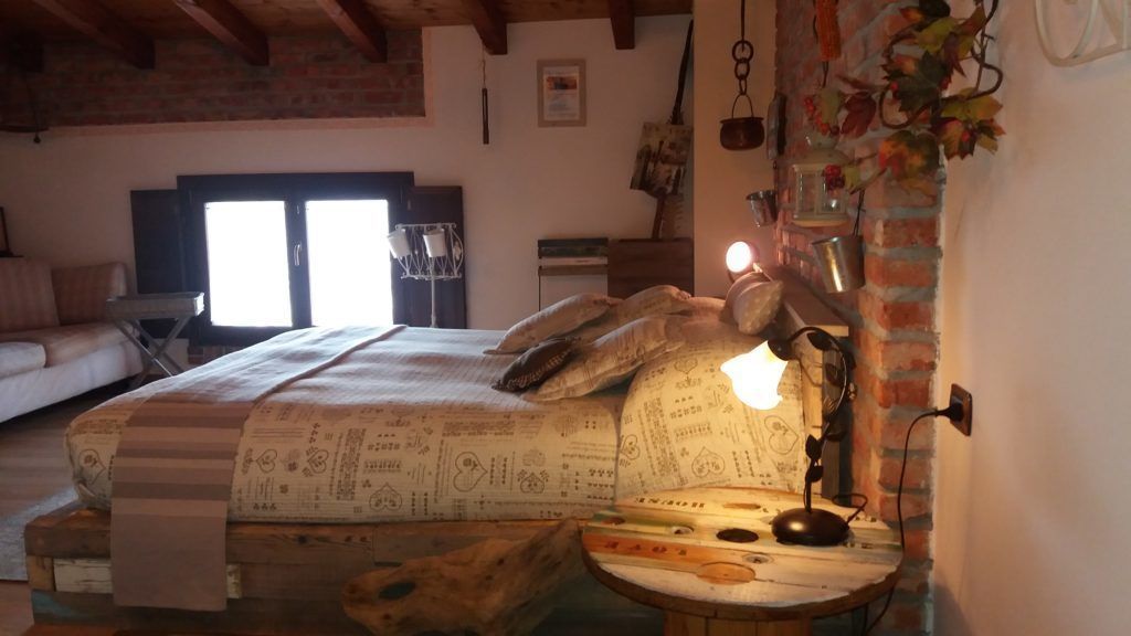 A rustic bedroom with a bed, a wooden nightstand, and a brick wall.
