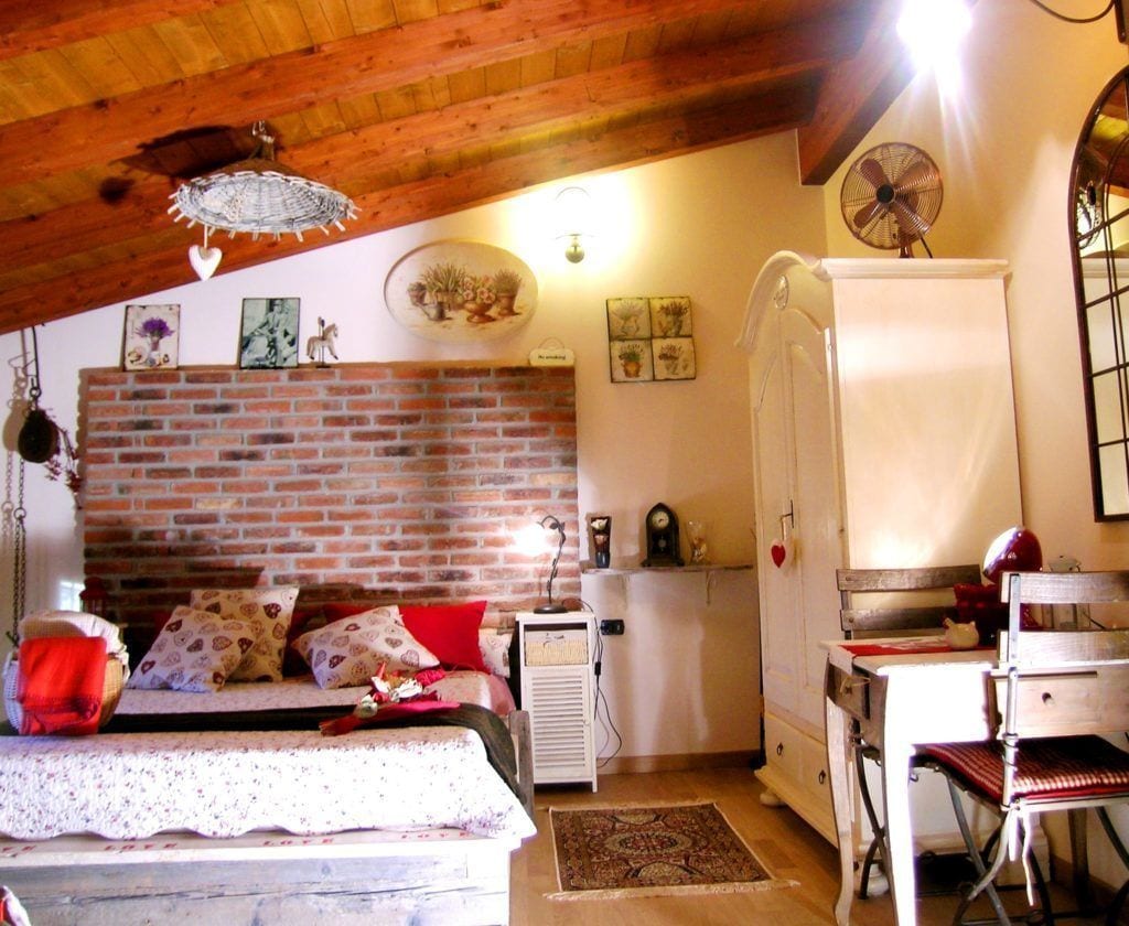 Ein gemütliches Zimmer mit Backsteinwand, einem Bett mit gemusterten Kissen, einem weißen Kleiderschrank und einem Schreibtisch mit Stuhl.