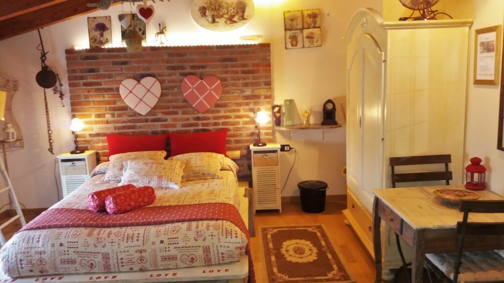 Un dormitorio acogedor con pared de ladrillo, una cama con ropa de cama roja y blanca, una mesita con una silla y un calentador.