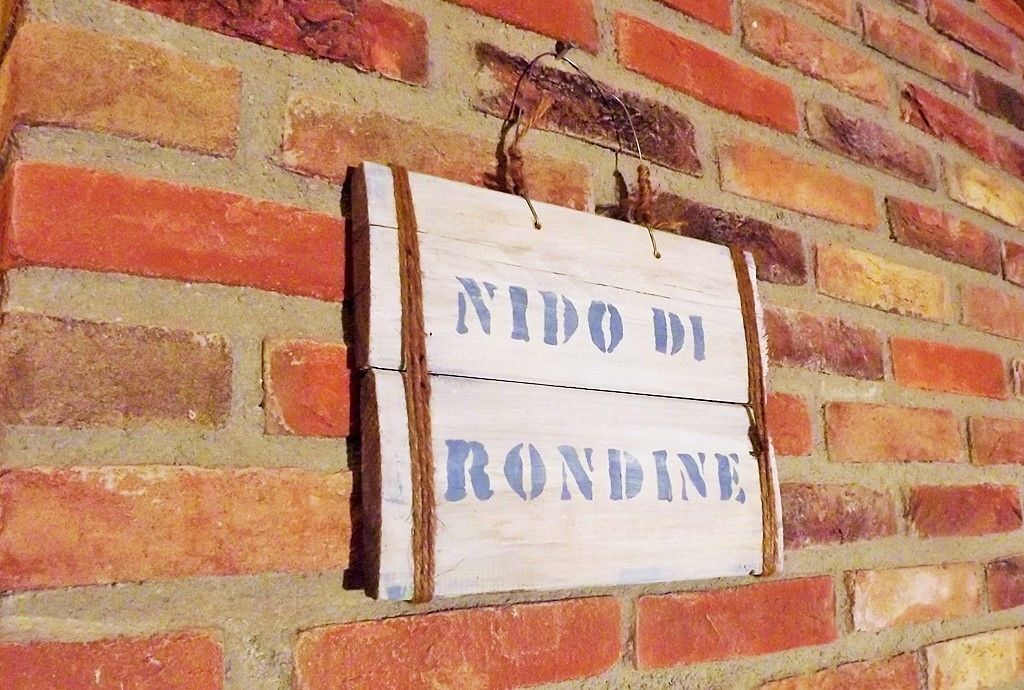 A wooden sign with the text "NIDO DI RONDINE" mounted on a brick wall.