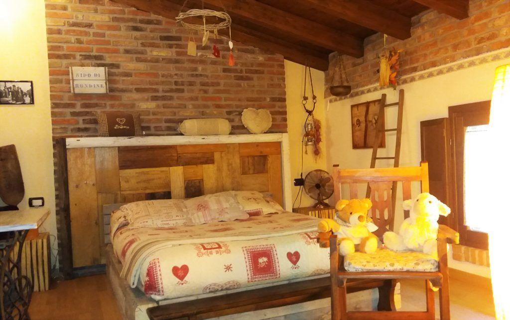 Una habitación acogedora con pared de ladrillo, cama de madera, una silla con peluches y un ventilador.