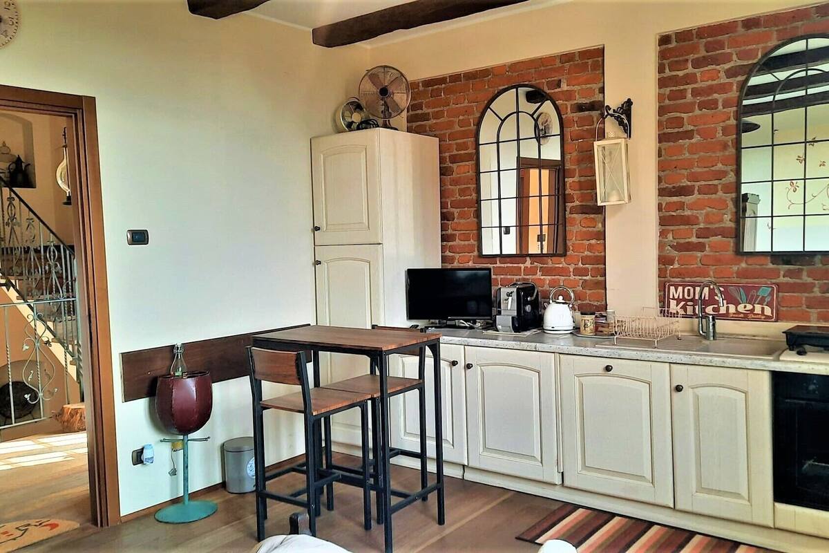 A kitchen with white cabinets, a wooden table, a TV, and a brick wall.