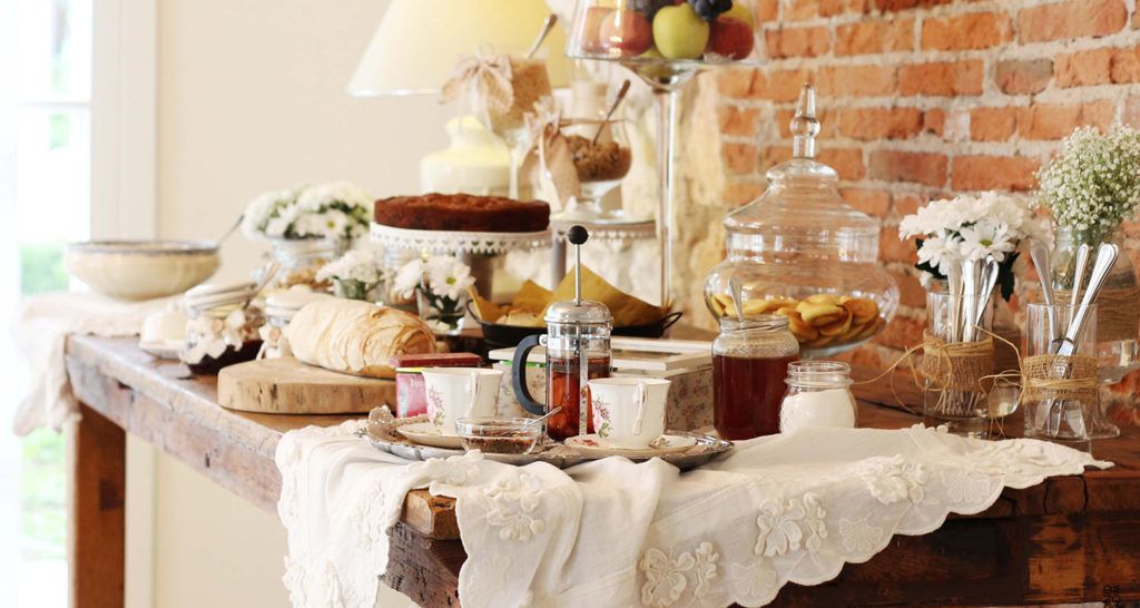 Ein reichhaltiges Frühstücksbuffet mit Speisen und Getränken auf einem Holztisch vor einer Ziegelwand.