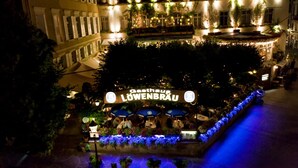 Un hôtel avec une enseigne indiquant « Gasthof LÖWENBRÄU », entouré de tables et de chaises en plein air, ainsi que de plantes.