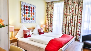 Une chambre d’hôtel avec un grand lit, des rideaux à motifs floraux, une œuvre d’art murale et une table de chevet avec une lampe.