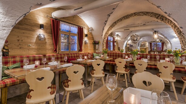 Un restaurant aux murs en bois, avec des sièges à carreaux rouges et blancs, des chaises en forme de cœur et une vue sur une rivière, visible à travers de grandes fenêtres.