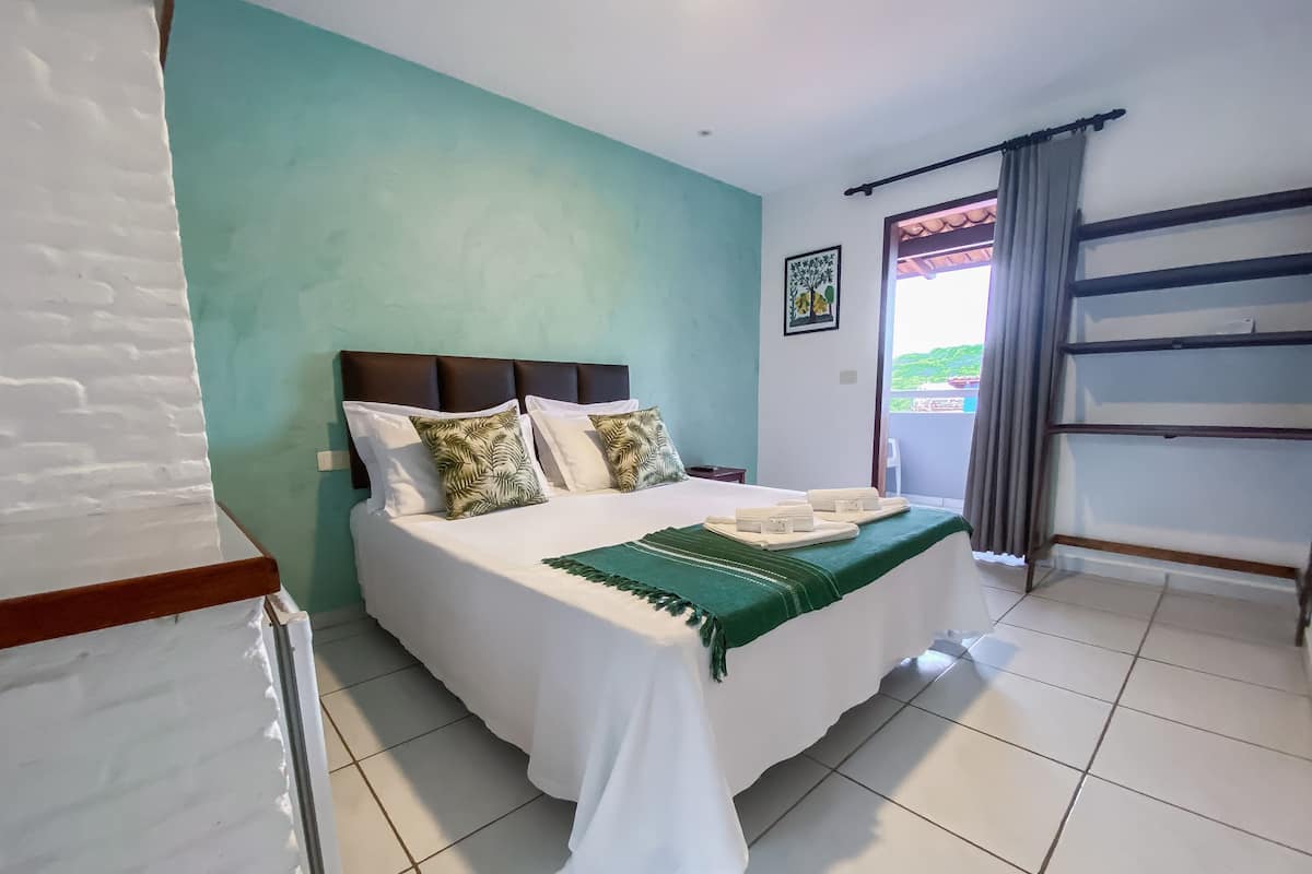 Una cama bien hecha con ropa blanca y almohadas verdes, una manta verde y un juego de toallas a un lado.