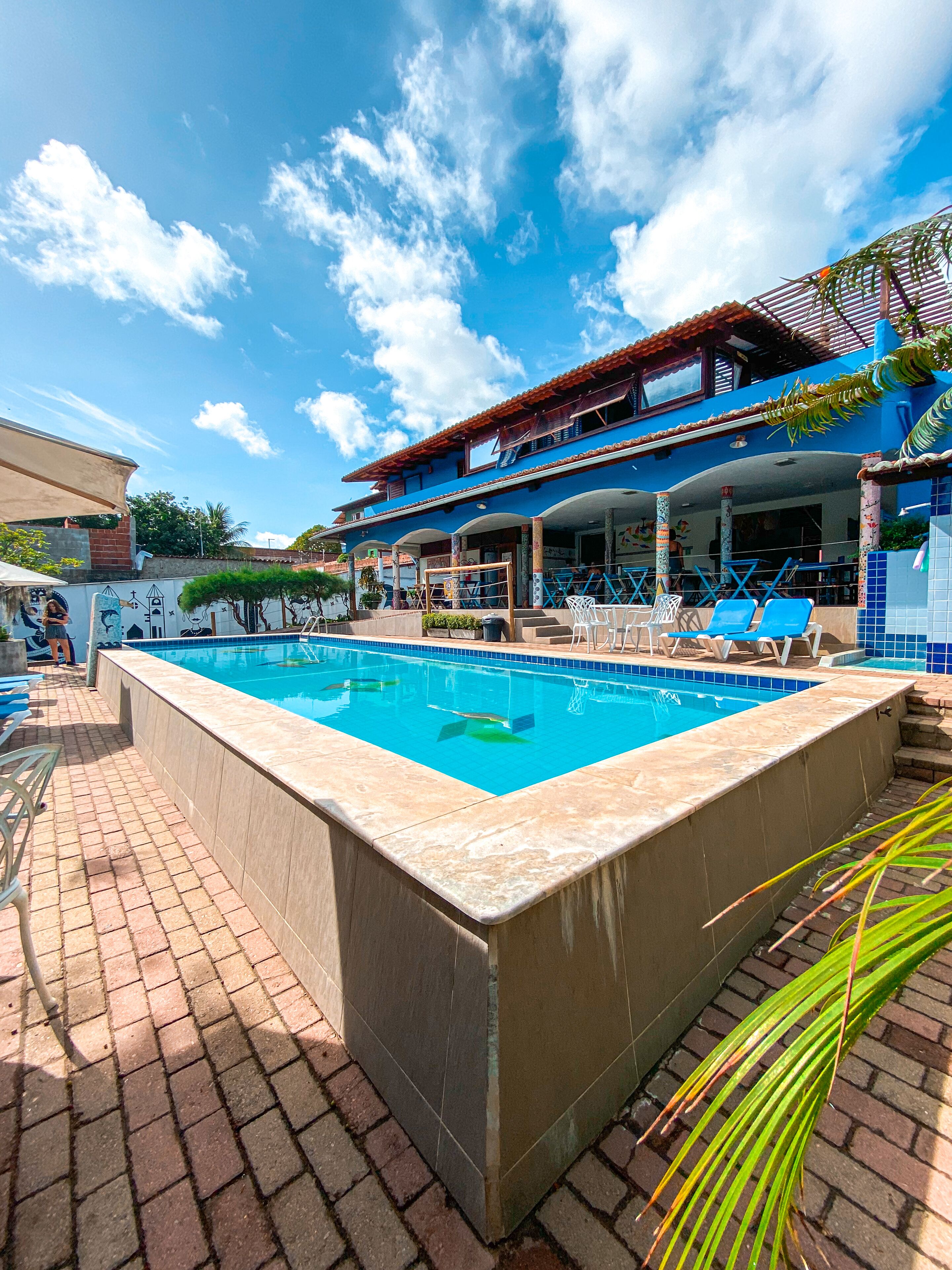 Une piscine avec des chaises longues, un patio couvert et un bâtiment à la façade bleue.