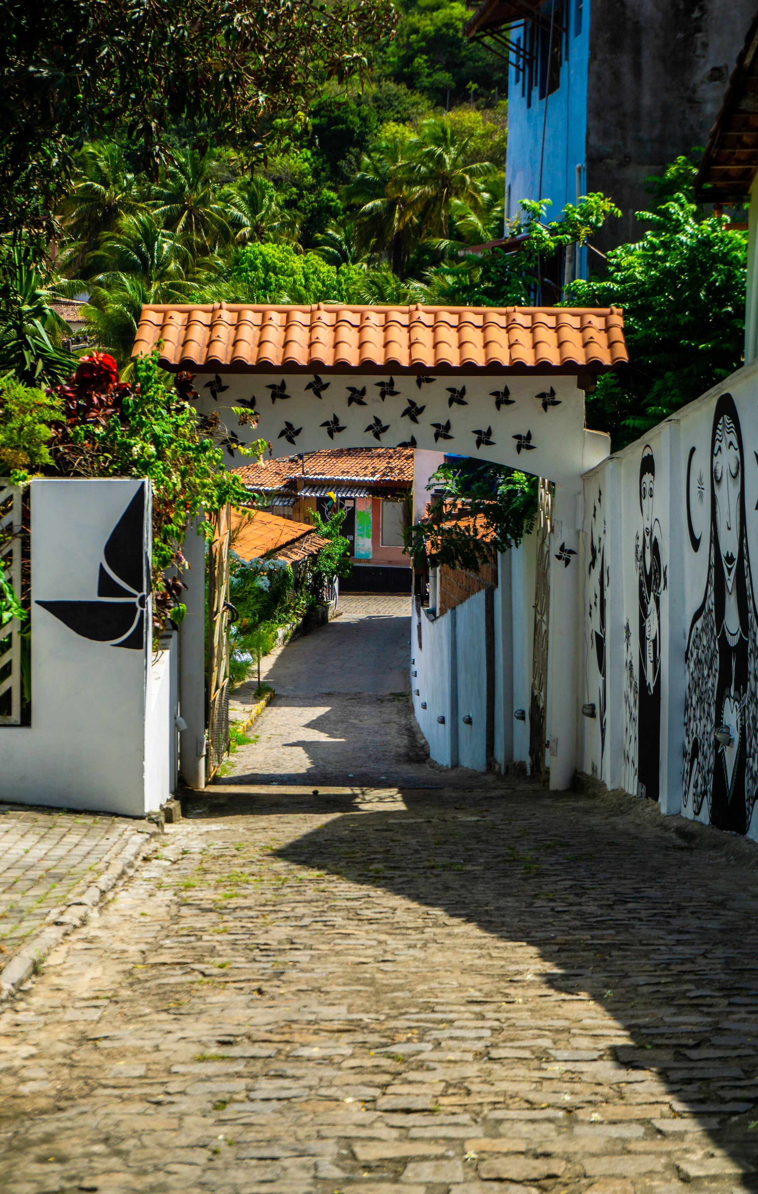 Una calle adoquinada que conduce a un edificio con tejado de tejas y un mural en la pared.