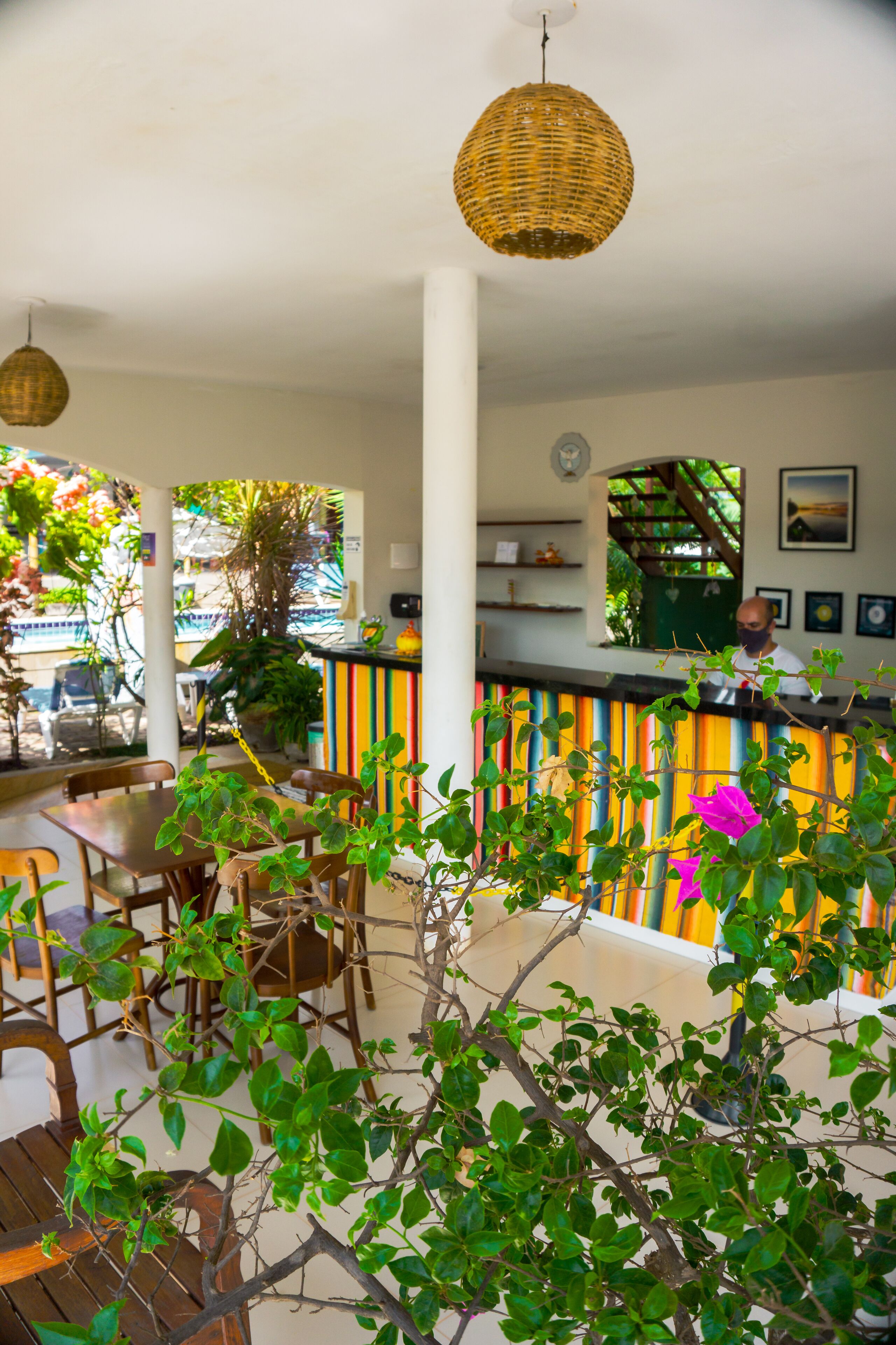Un restaurante con zona de bar, mesas y sillas de madera, y lámparas colgantes de mimbre.