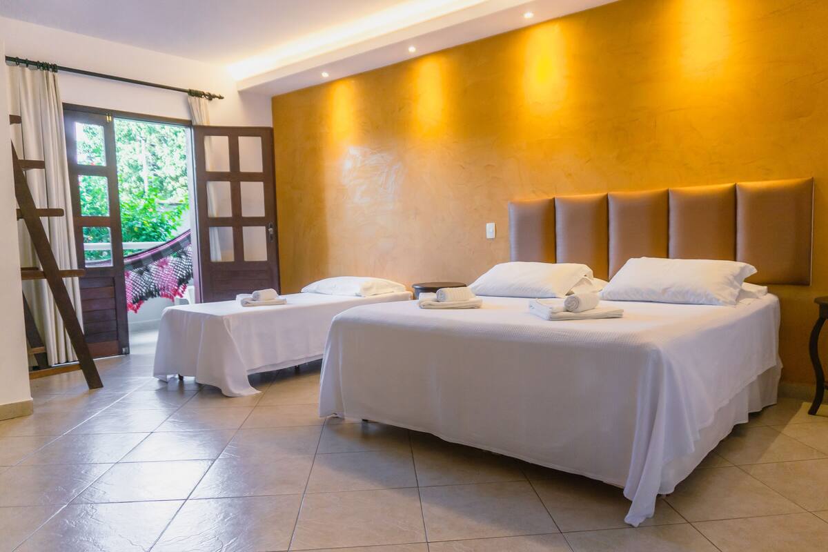 Habitación de hotel con dos camas, cabecero de madera y vistas a zonas verdes a través de una puerta.