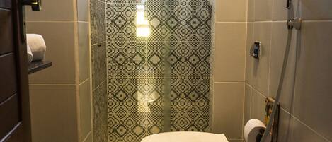 Un baño con inodoro, ducha y pared de azulejos estampados.