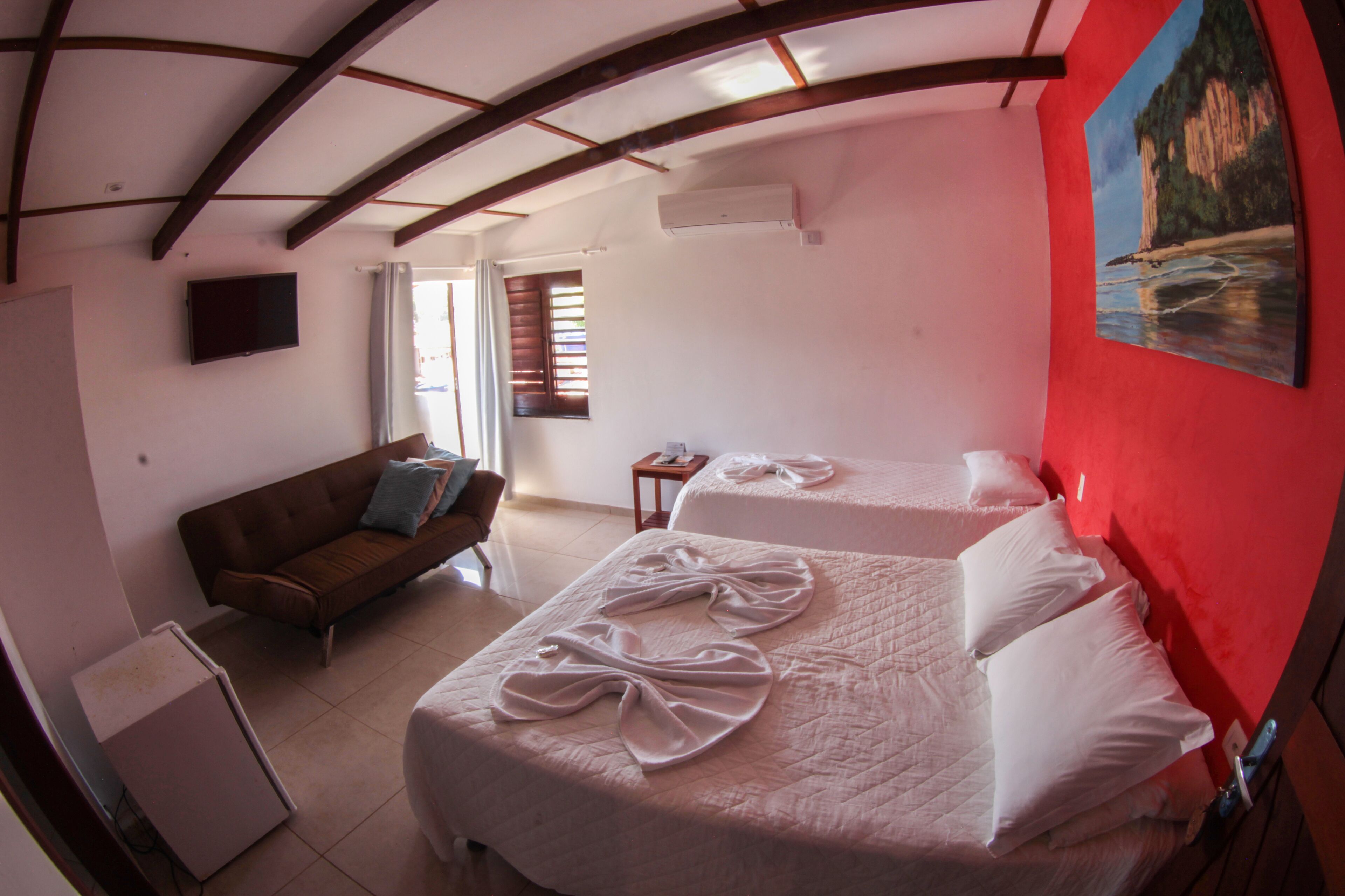 A hotel room with two beds, a sofa, a TV, and a painting on the wall.
