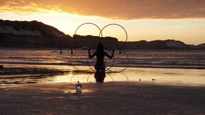 Une scène de plage où l’on voit une personne jouer avec des cerceaux, un ciel dégagé et des montagnes au loin.