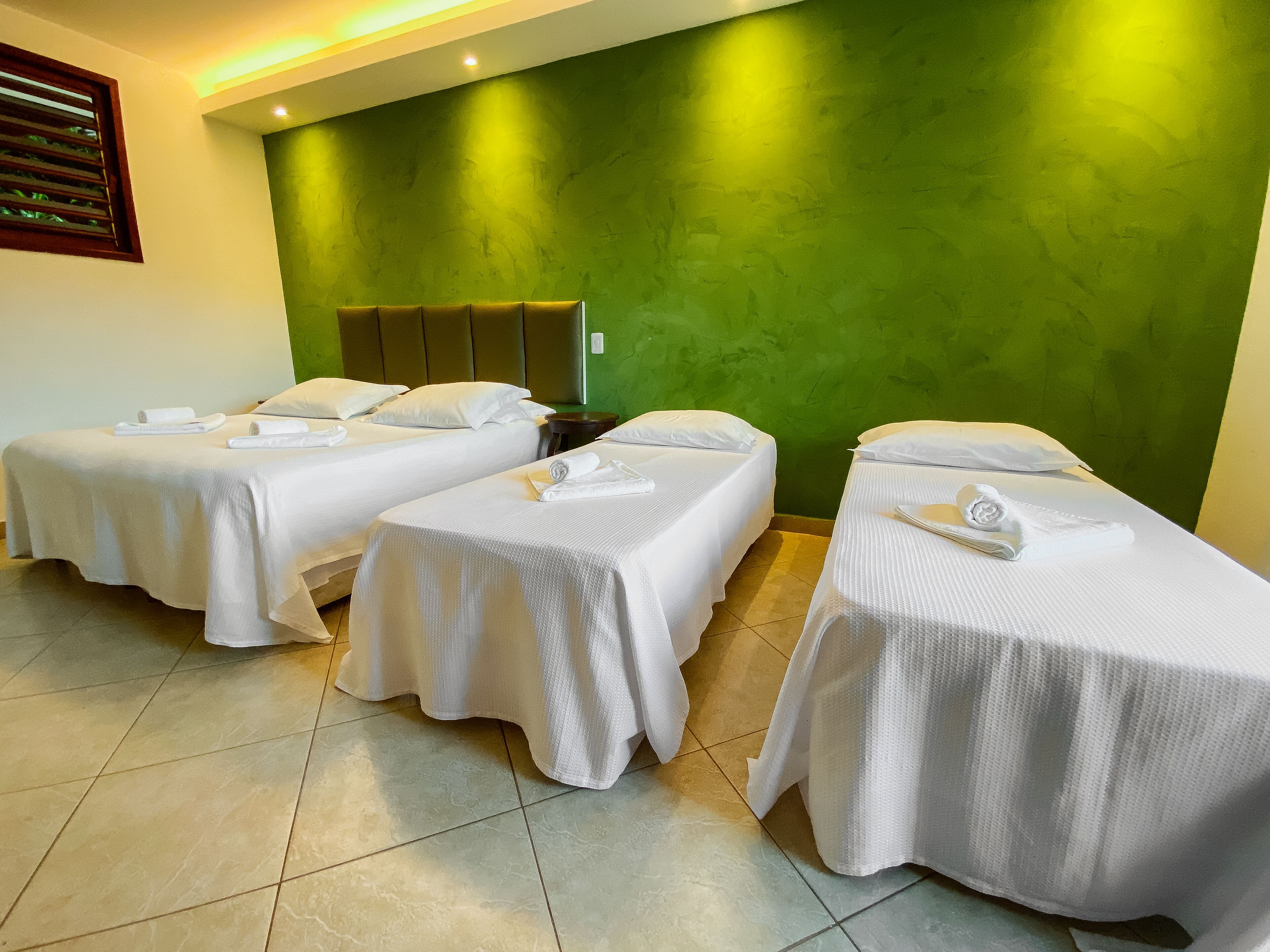 Habitación de hotel con dos camas individuales, una pared verde de acento y un cabecero de madera.