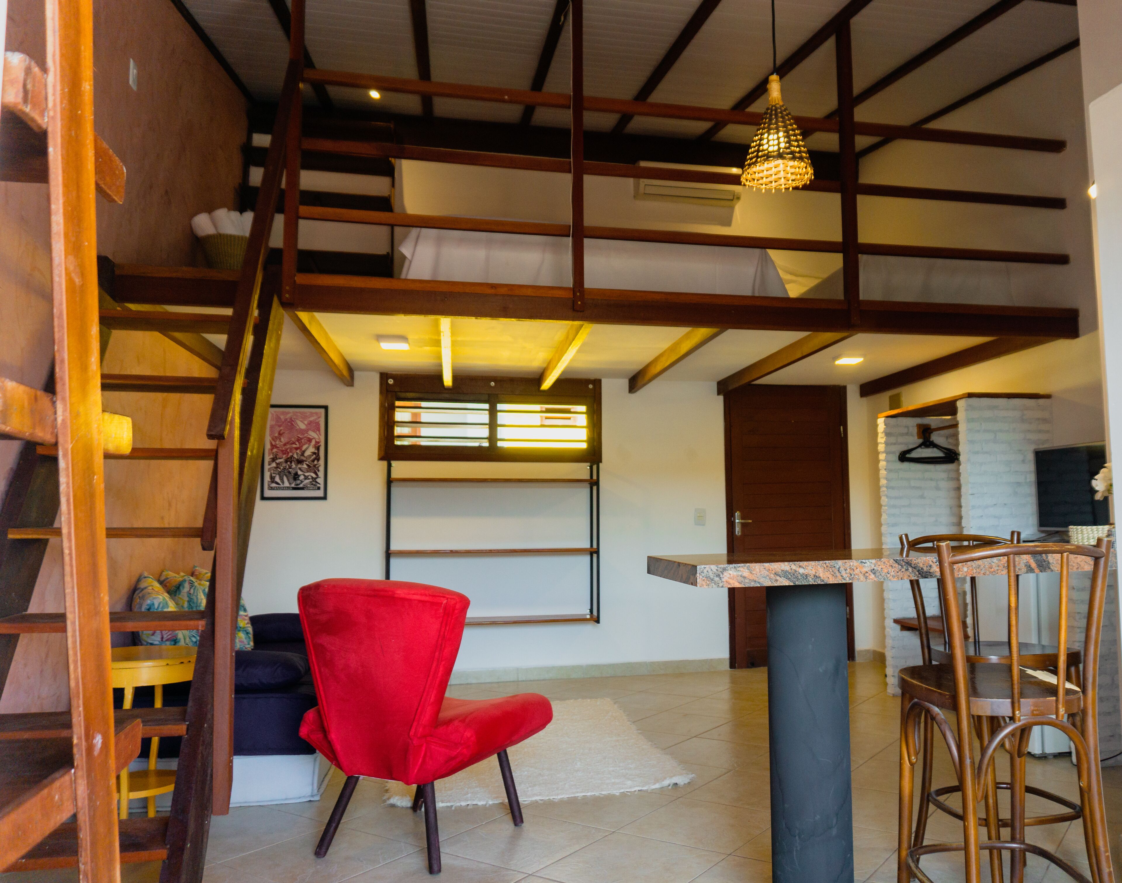 Un salón amplio con una silla roja, una escalera de madera y una cocina con una lámpara colgante.