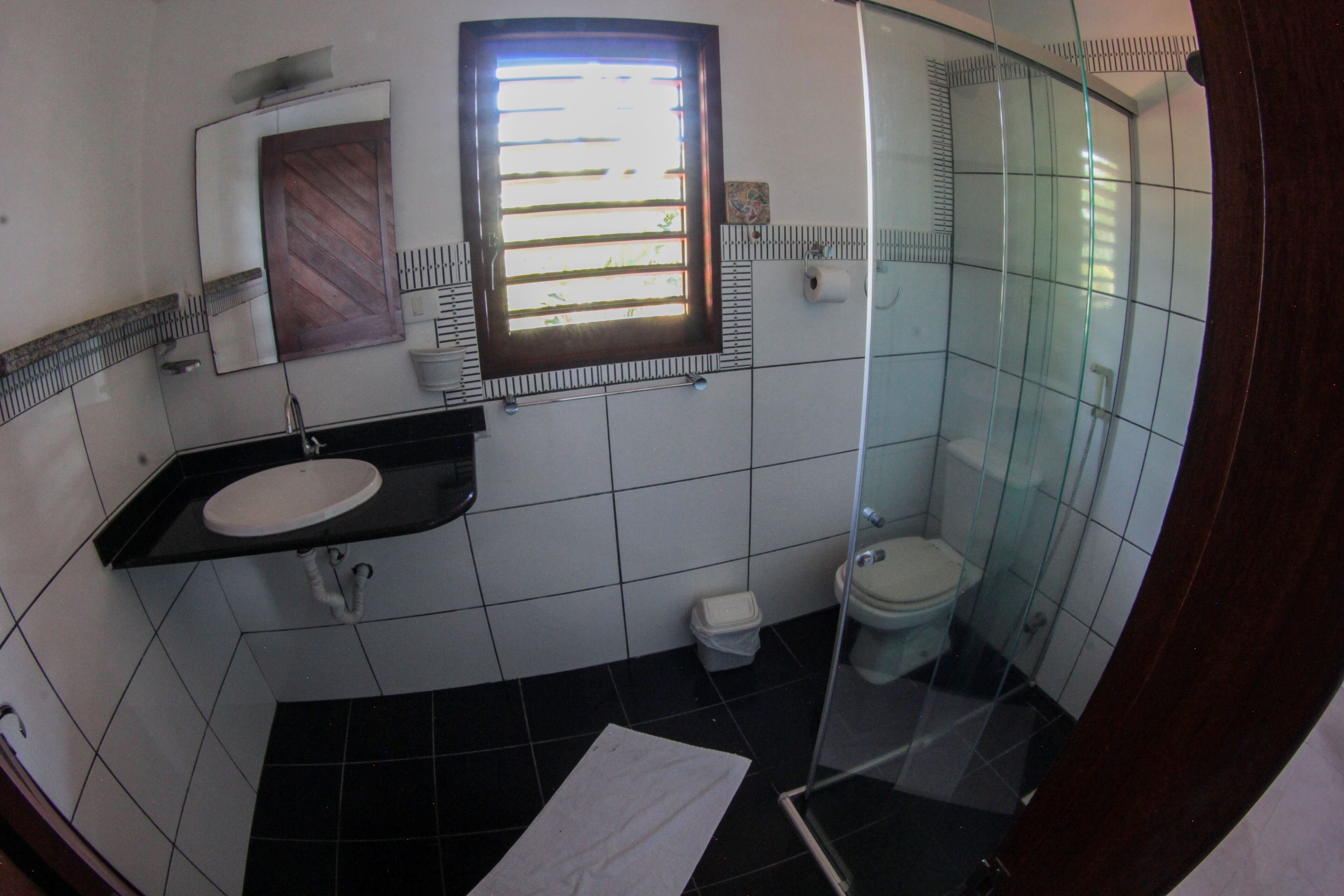 A bathroom with a black tiled floor, a white sink, a toilet, and a glass shower enclosure.