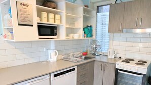 A modern kitchen with white cabinetry, a built-in microwave, a stove, and a dishwasher. - Highfield Hotel (Potts Point)
