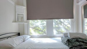 A bedroom with a bed, a window with a view of trees, and a white wall. - Highfield Hotel (Potts Point)