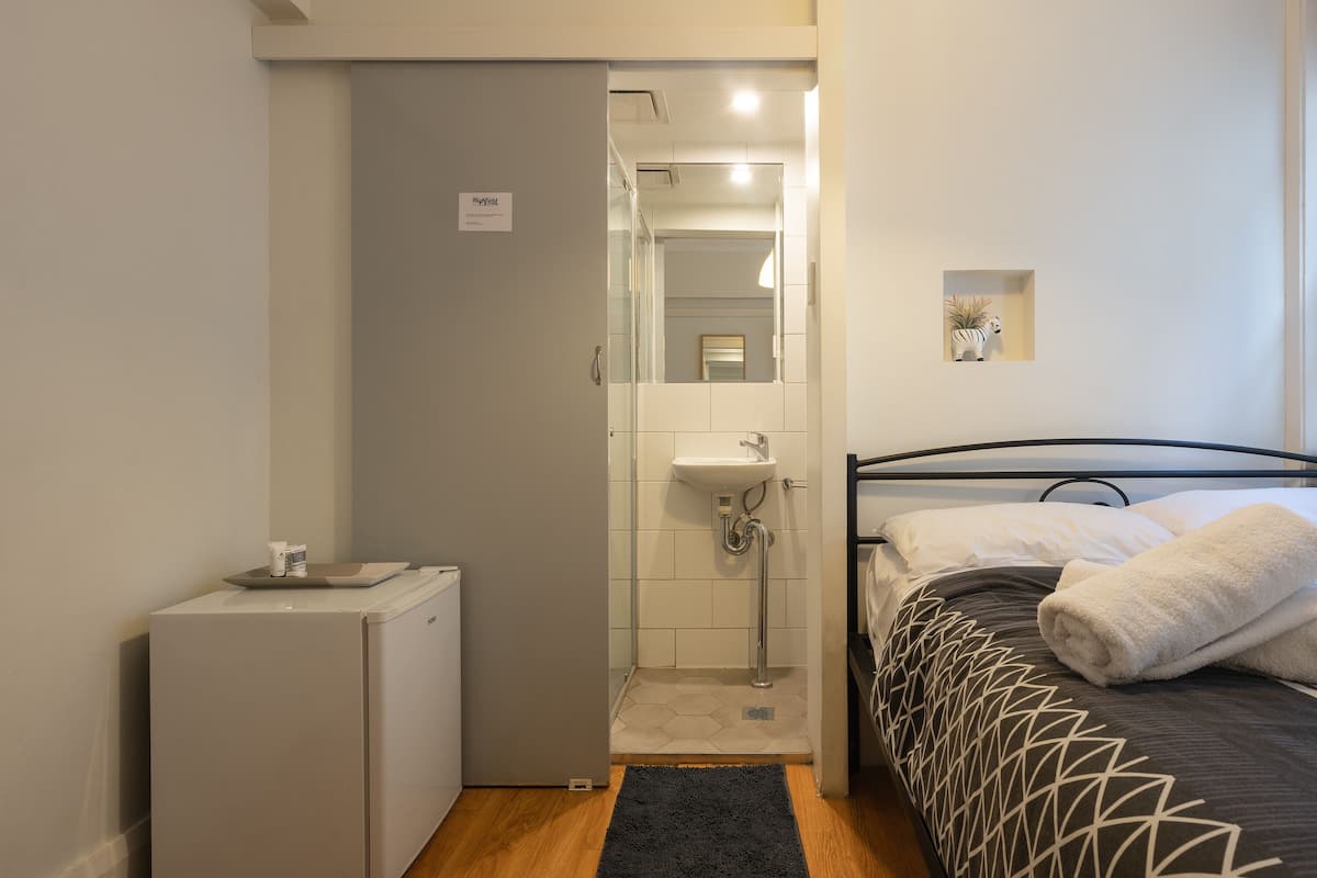 Habitación de hotel pequeña con cama, mesita de noche, lavabo integrado y refrigerador compacto.