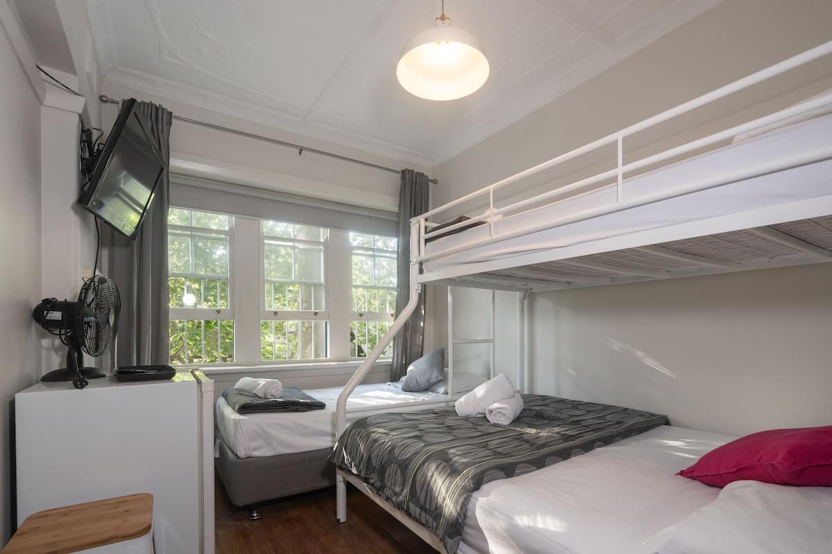 Una habitación con literas, un escritorio, una silla, un ventilador y una ventana con cortinas.