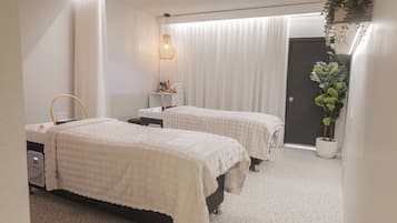 A hotel room with two beds, a bedside table, a lamp, a potted plant, and a door.