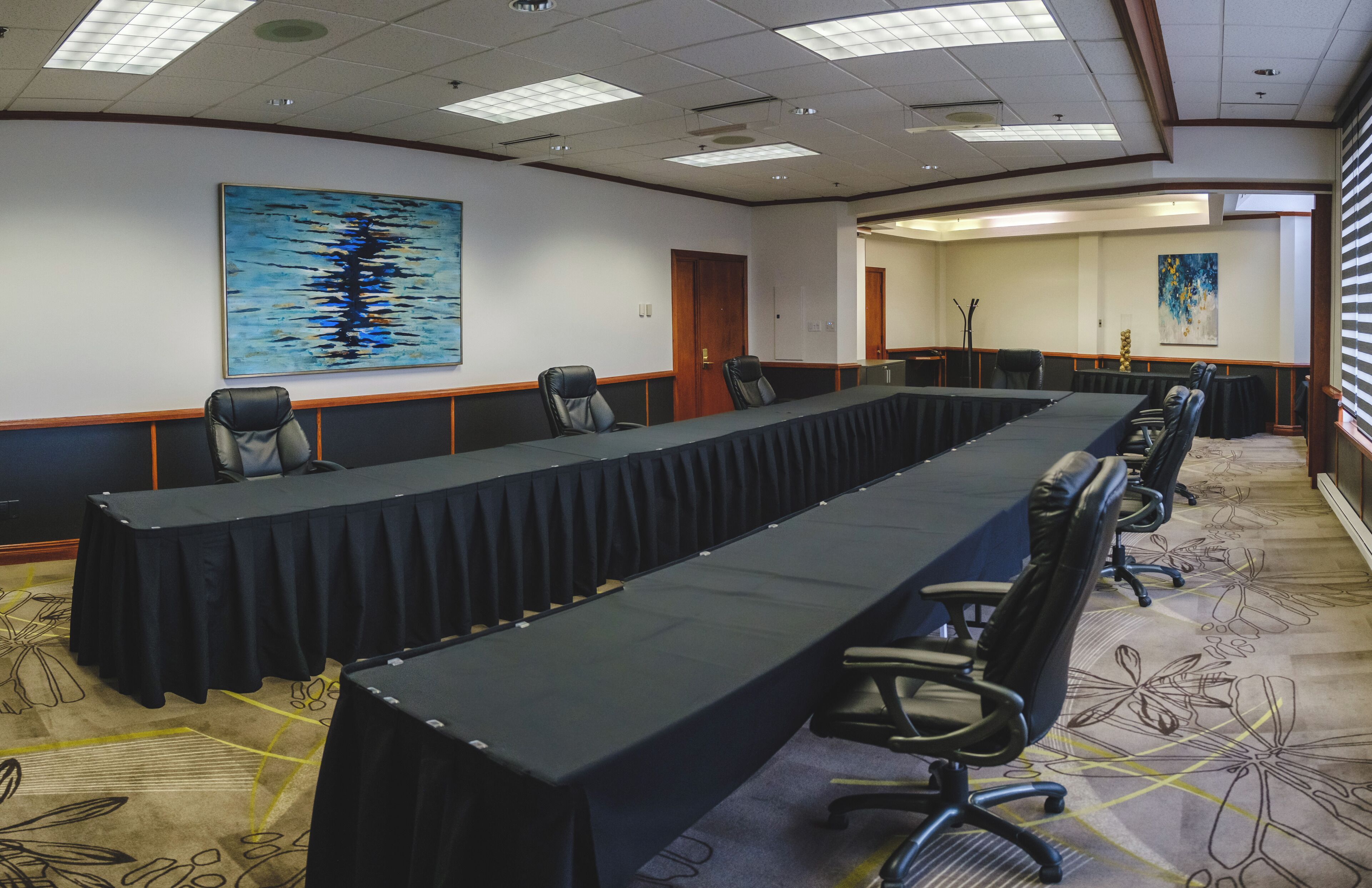 A conference room with a long table, chairs, and two paintings on the walls.