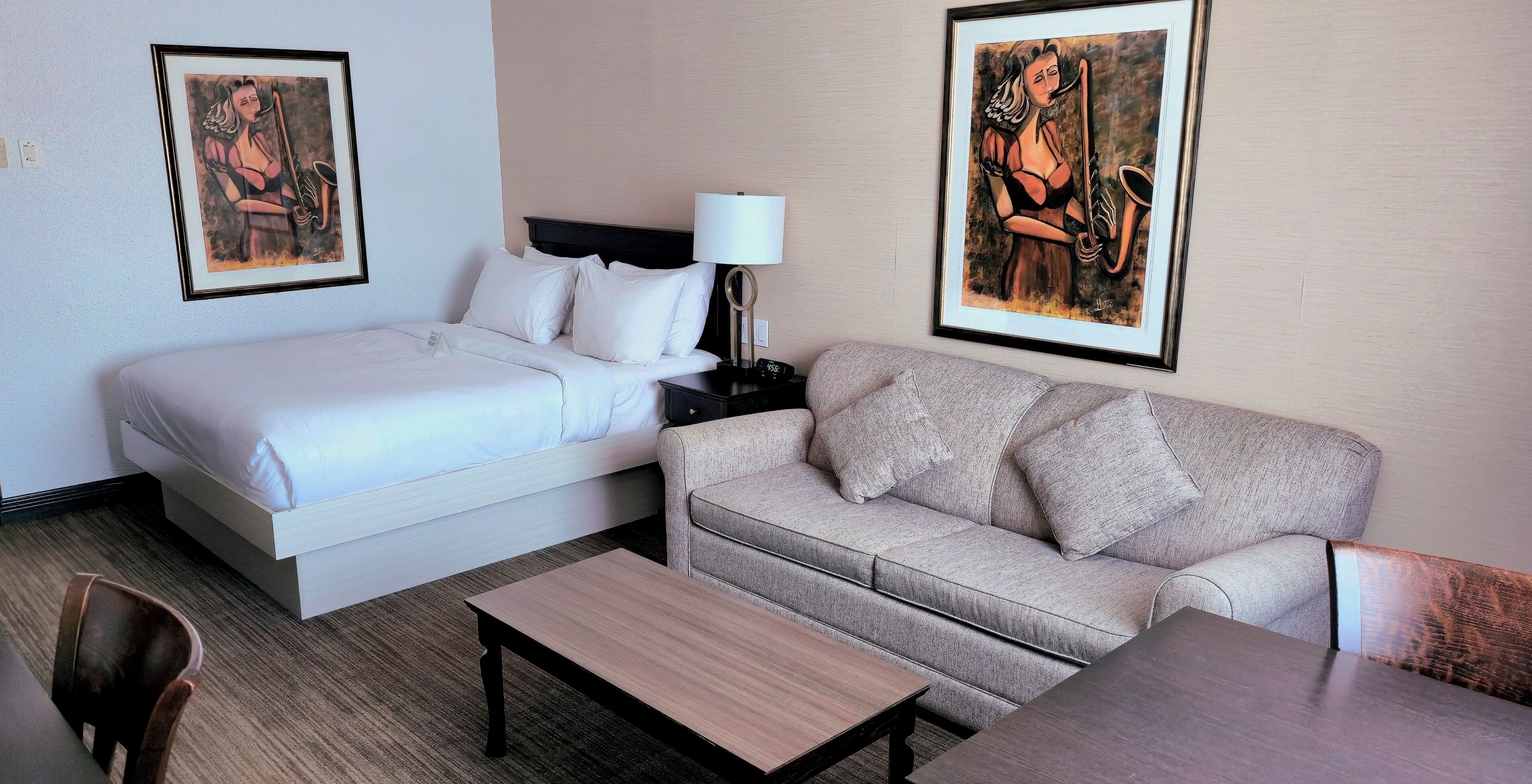 Habitación de hotel con cama, sofá, mesa y dos cuadros en las paredes.