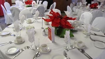 Uma sala de banquetes com mesas redondas montadas para um evento formal, com toalhas brancas, talheres e centros de mesa com flores de poinsétia vermelhas.