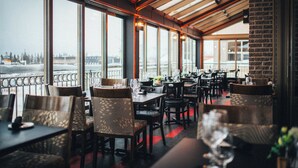 A restaurant with a view of a snowy landscape through large windows. Tables are arranged with chairs, and the interior has a modern design with a wooden ceiling. - Le Montagnais (Saguenay)