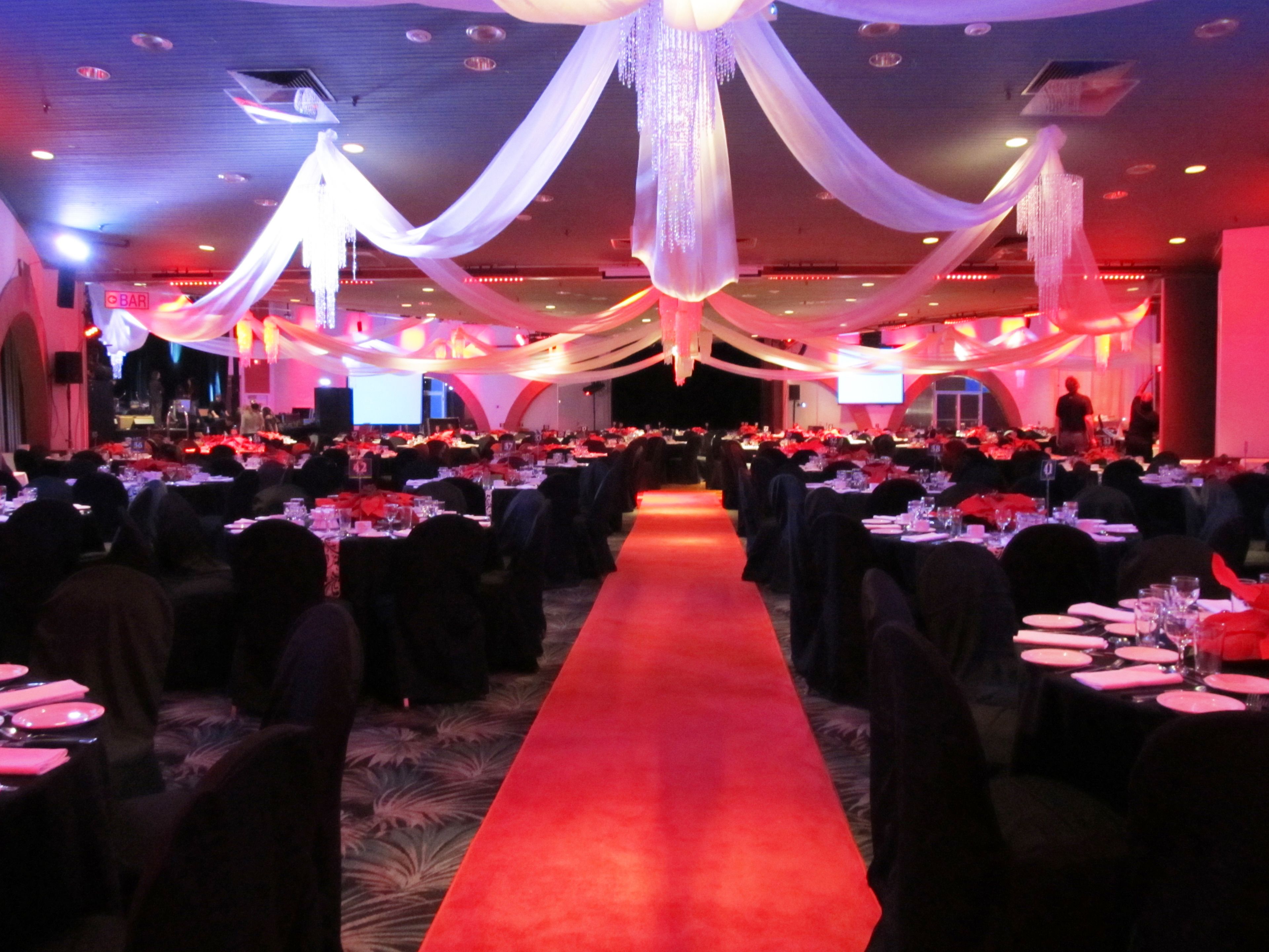 A banquet hall with tables arranged in rows, a red carpet, and draped white fabric from the ceiling.