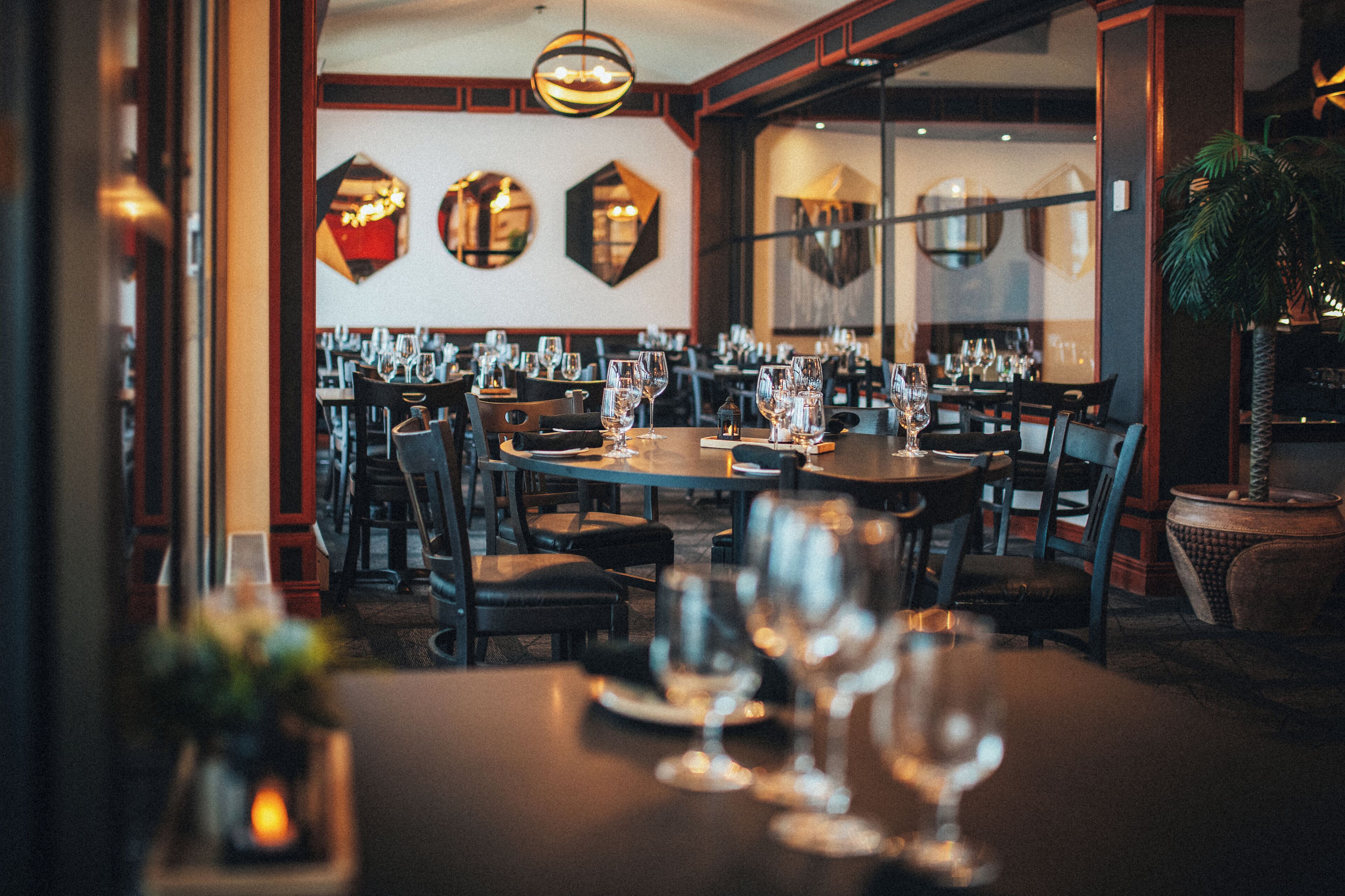 Un restaurante con varias mesas y sillas, cada conjunto con copas de vino y platos.